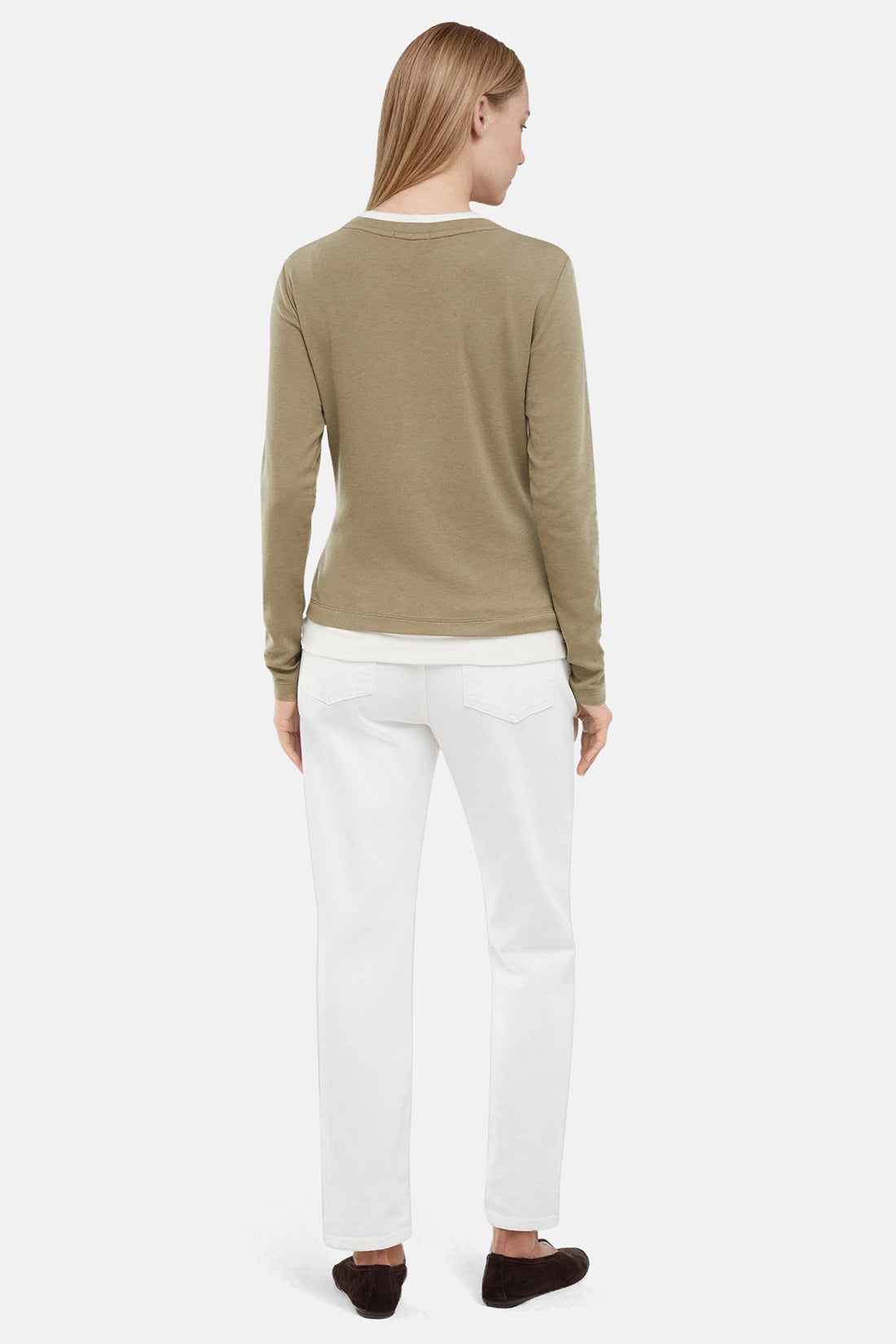 Back of woman wearing a green sweater with white layered hem and white pants on a light gray background.