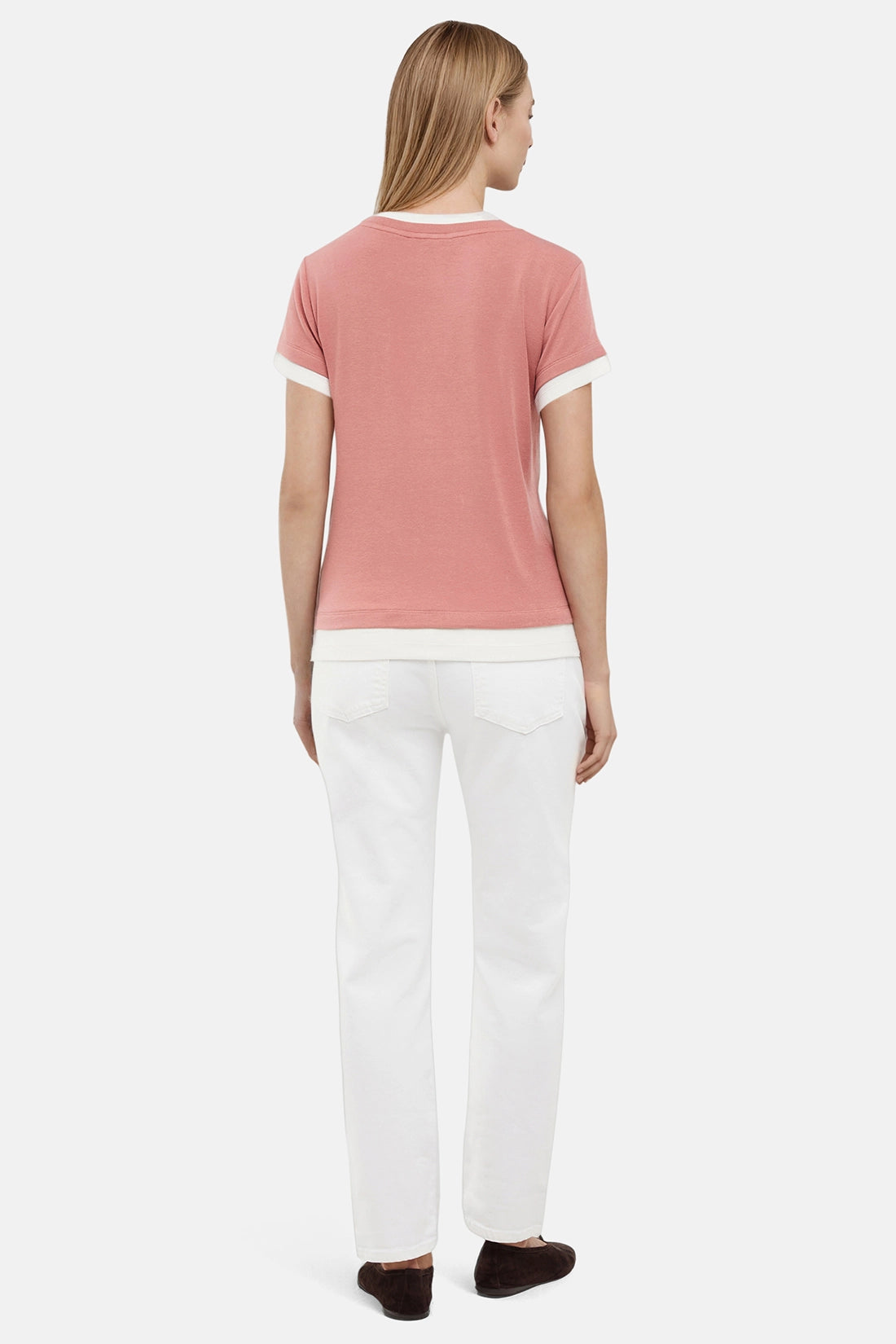 Back of woman wearing a pink tee with white layered hem and white pants on a light gray background