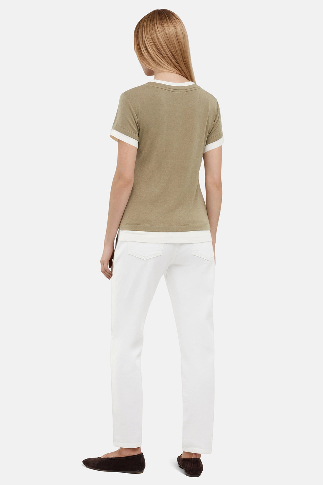 Back of woman wearing a green tee with white layered hem and white pants on a light gray background