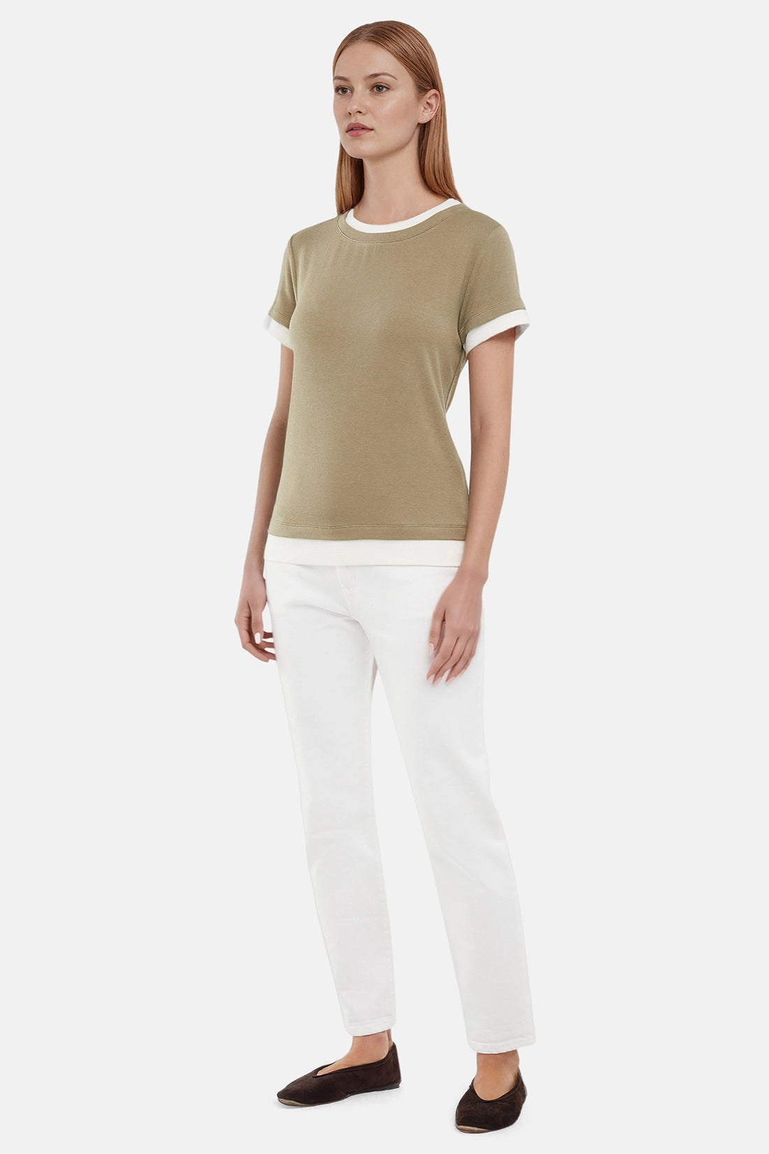 Side of woman wearing a green tee with white layered hem and white pants on a light gray background