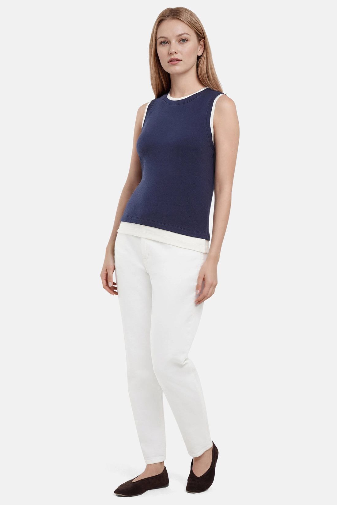 Front of woman wearing a navy tank with white layered hem and white pants on a light gray background.