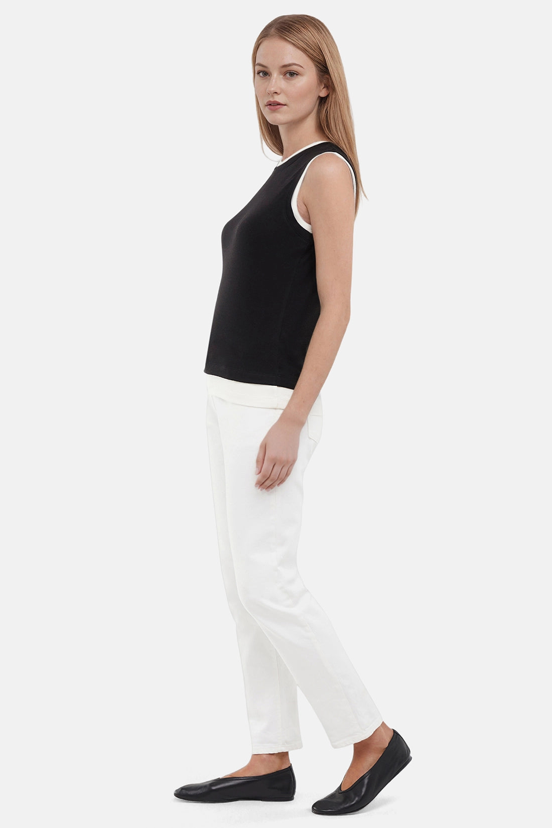 Side view of woman wearing a navy black with white layered hem and white pants on a light gray background.