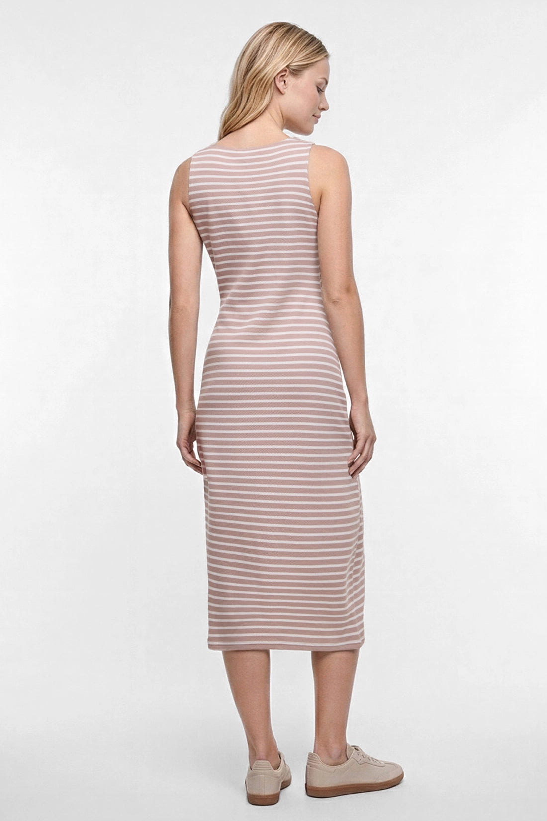 A woman shown from the back wearing a sleeveless midi dress with thin horizontal light brown and white stripes, paired with beige sneakers, against a plain white studio background.