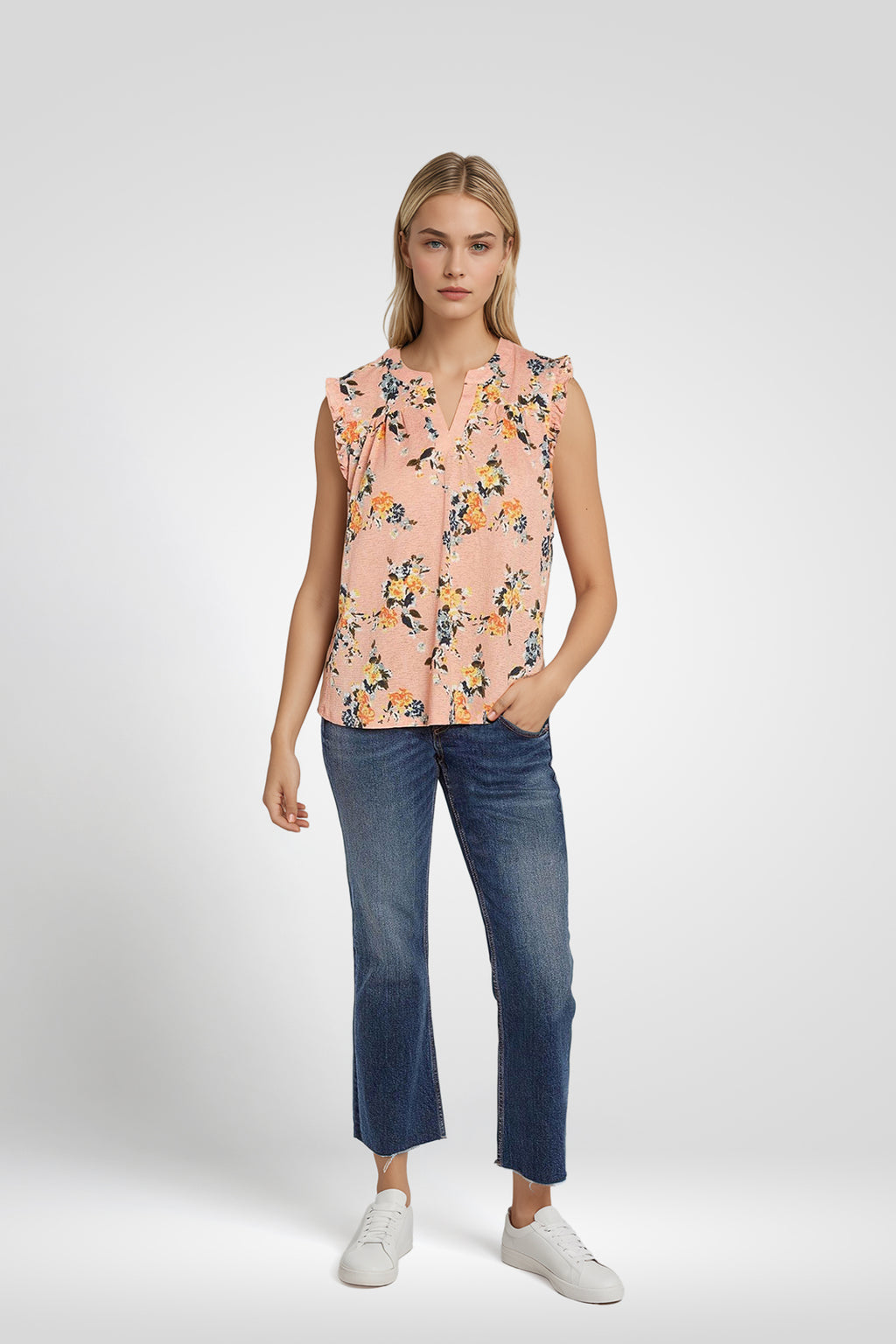 Woman wearing a sleeveless floral blouse and blue jeans with a plain background. coral-pink-yarrow