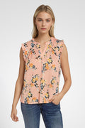 Woman wearing a sleeveless floral blouse and blue jeans with a plain background. coral-pink-yarrow