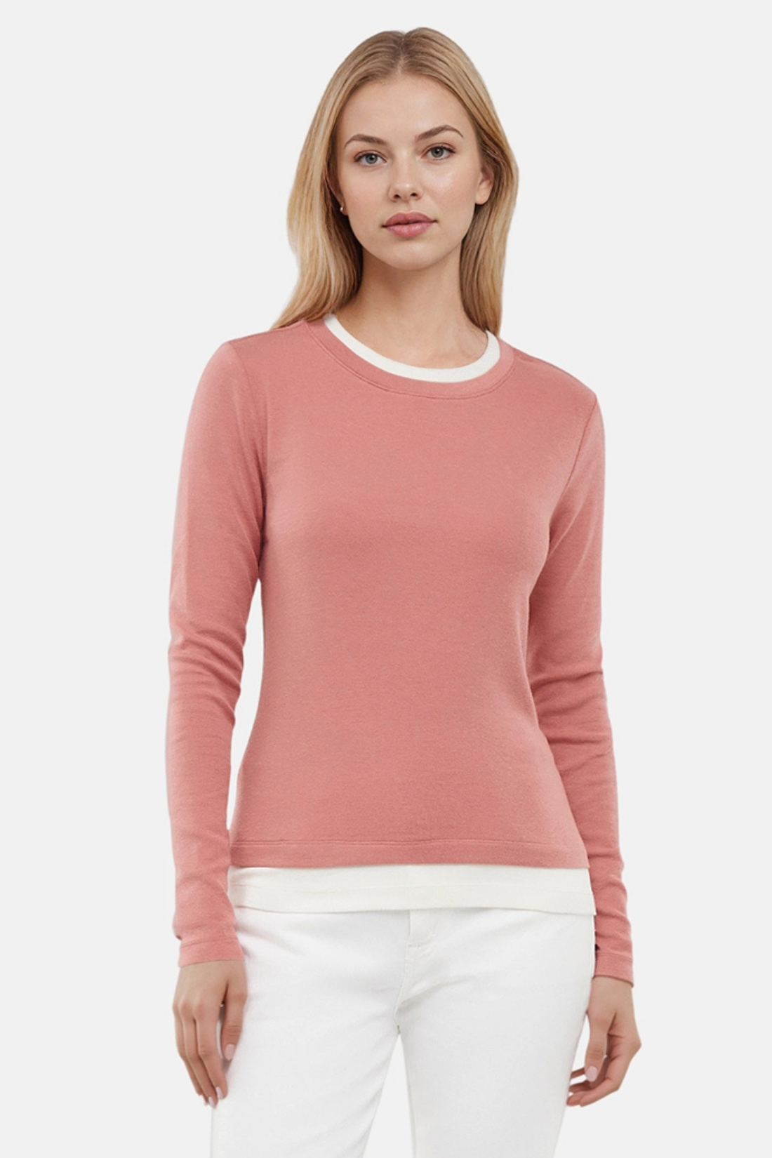 Woman wearing a pink sweater with white layered hem and white pants on a light gray background.