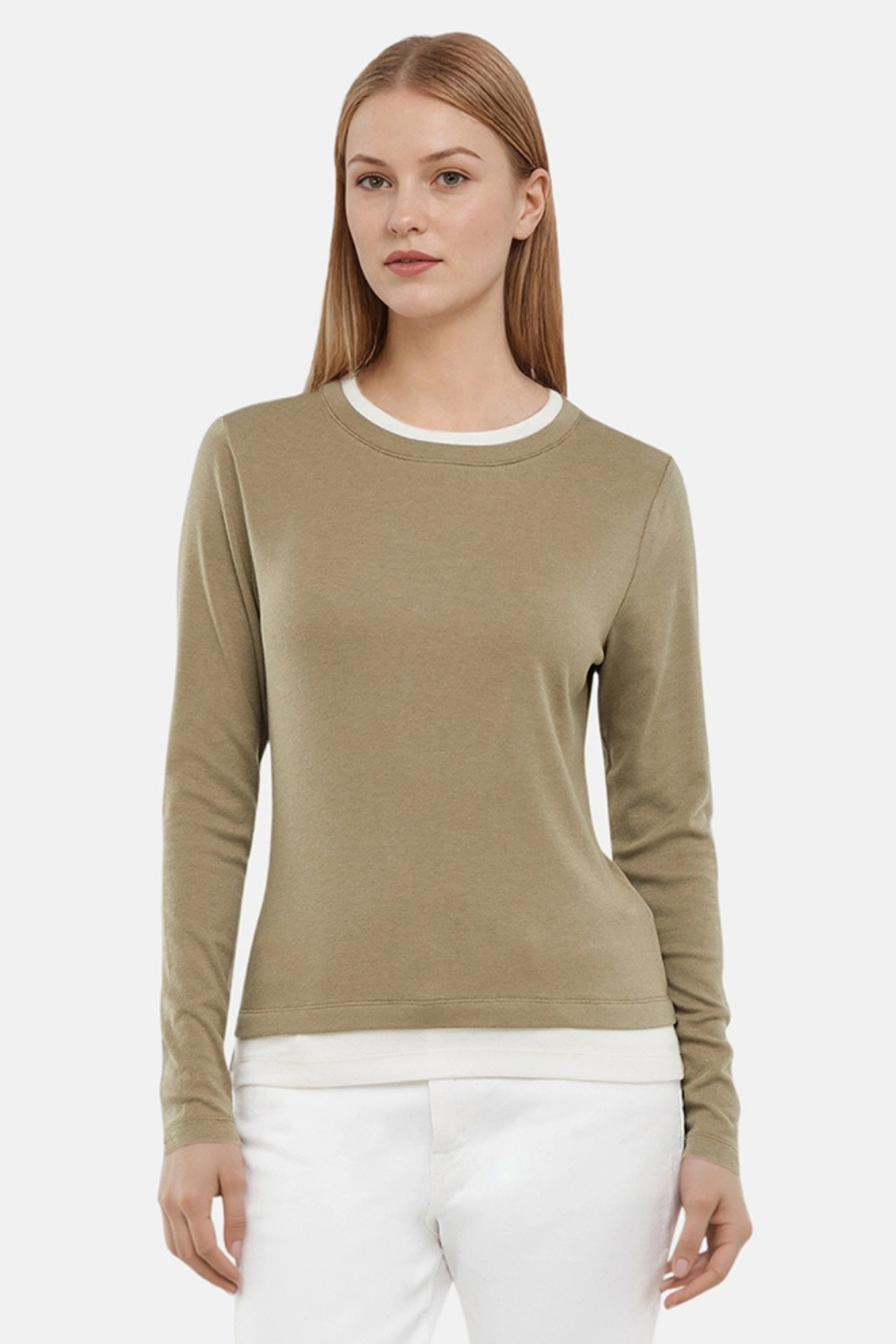 Woman wearing a green sweater with white layered hem and white pants on a light gray background. 