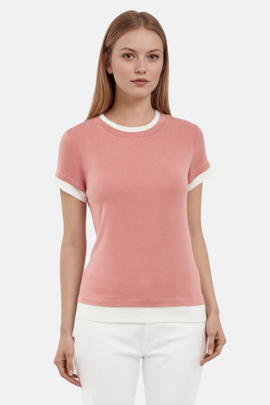 Woman wearing a pink tee with white layered hem and white pants on a light gray background 