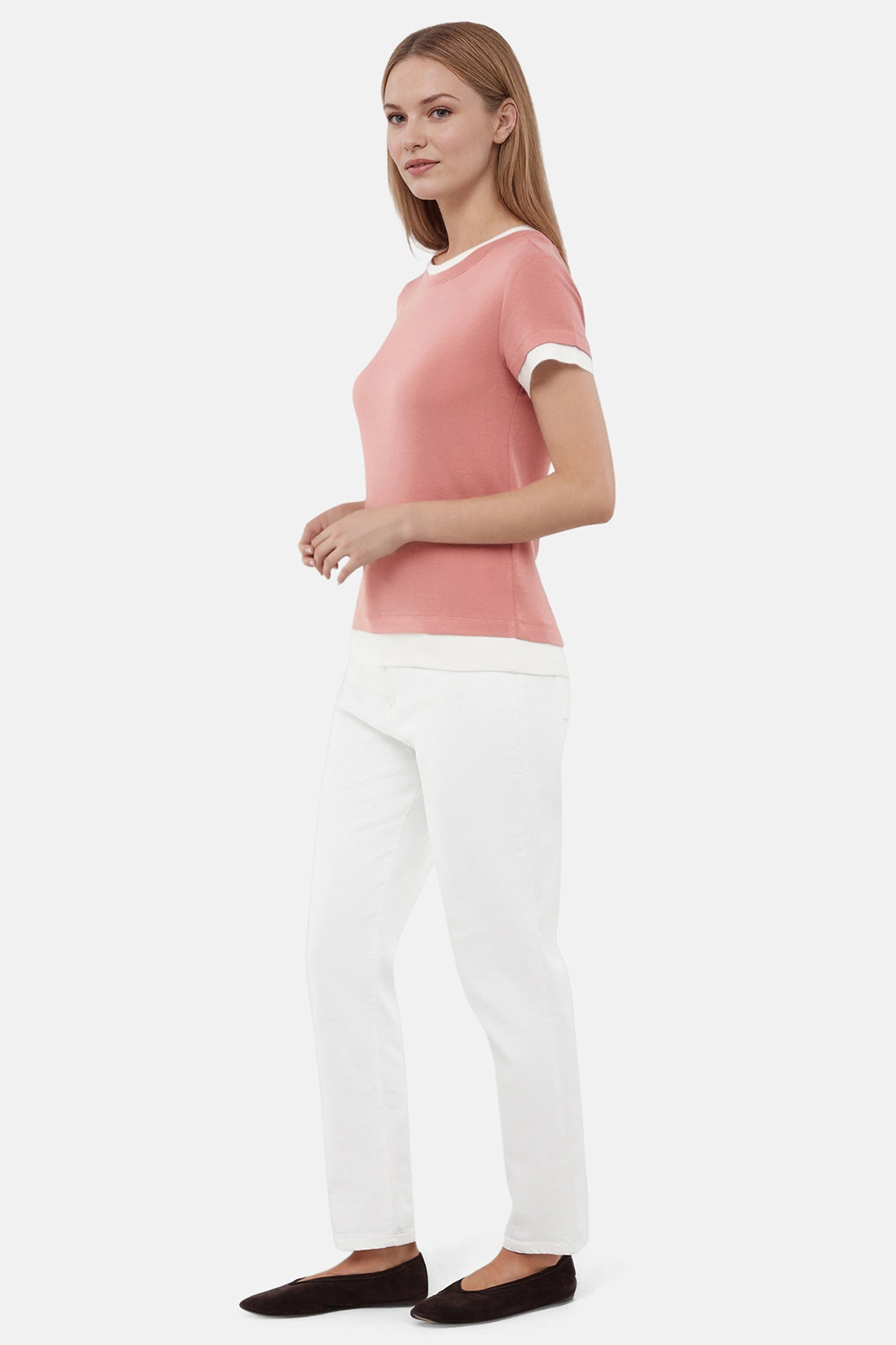 Side view of woman wearing a pink tee with white layered hem and white pants on a light gray background 