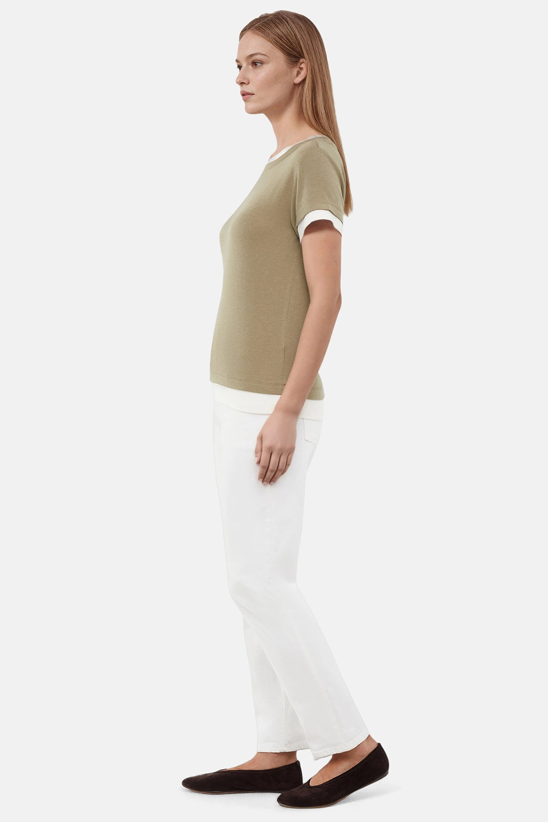 Side of woman wearing a green tee with white layered hem and white pants on a light gray background 