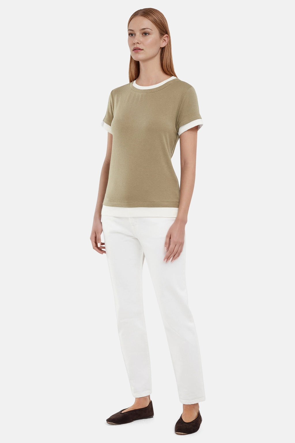 Side of woman wearing a green tee with white layered hem and white pants on a light gray background #color_deep-lichen-green