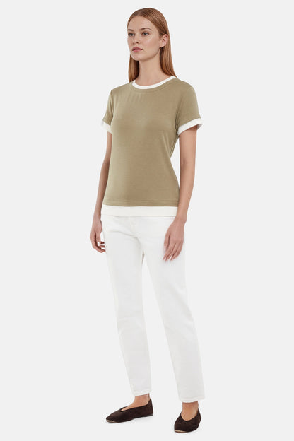 Side of woman wearing a green tee with white layered hem and white pants on a light gray background 