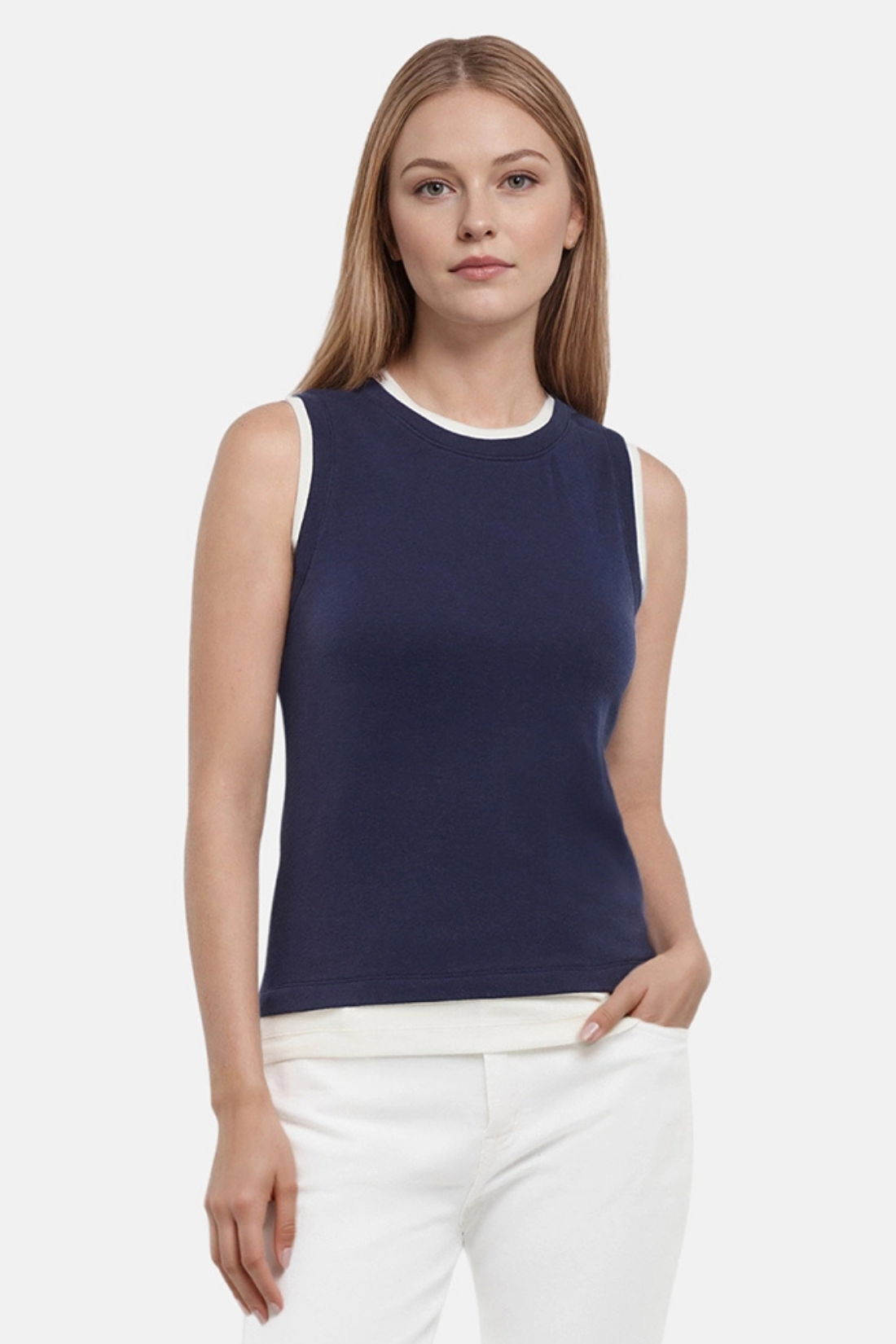 Front of woman wearing a navy tank with white layered hem and white pants on a light gray background. 