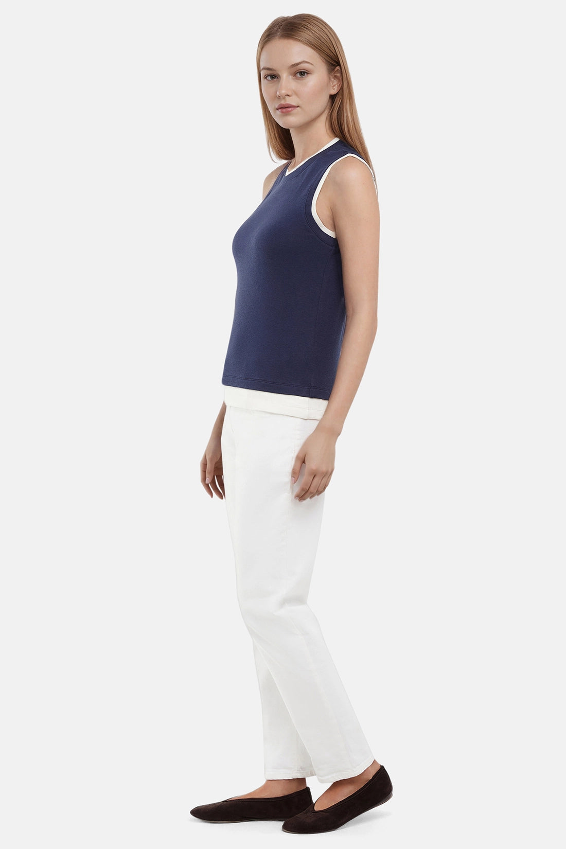 Side of woman wearing a navy tank with white layered hem and white pants on a light gray background. 