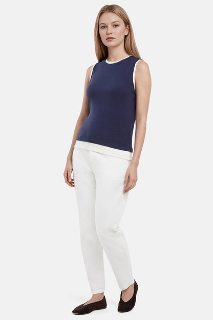 Front of woman wearing a navy tank with white layered hem and white pants on a light gray background. 