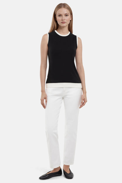 Front of woman wearing a navy black with white layered hem and white pants on a light gray background. 