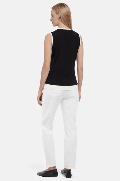 Back of woman wearing a navy black with white layered hem and white pants on a light gray background. 