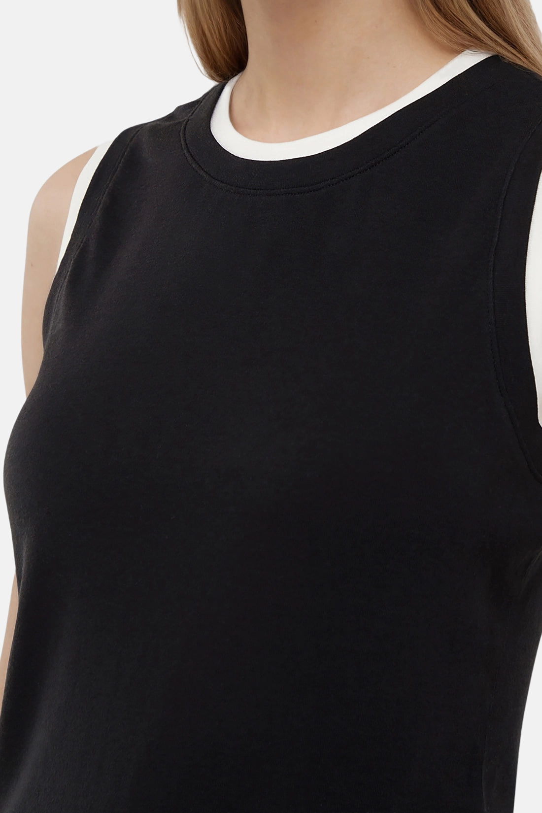 Close up of woman wearing a black tank with white layered hem on a light gray background. 