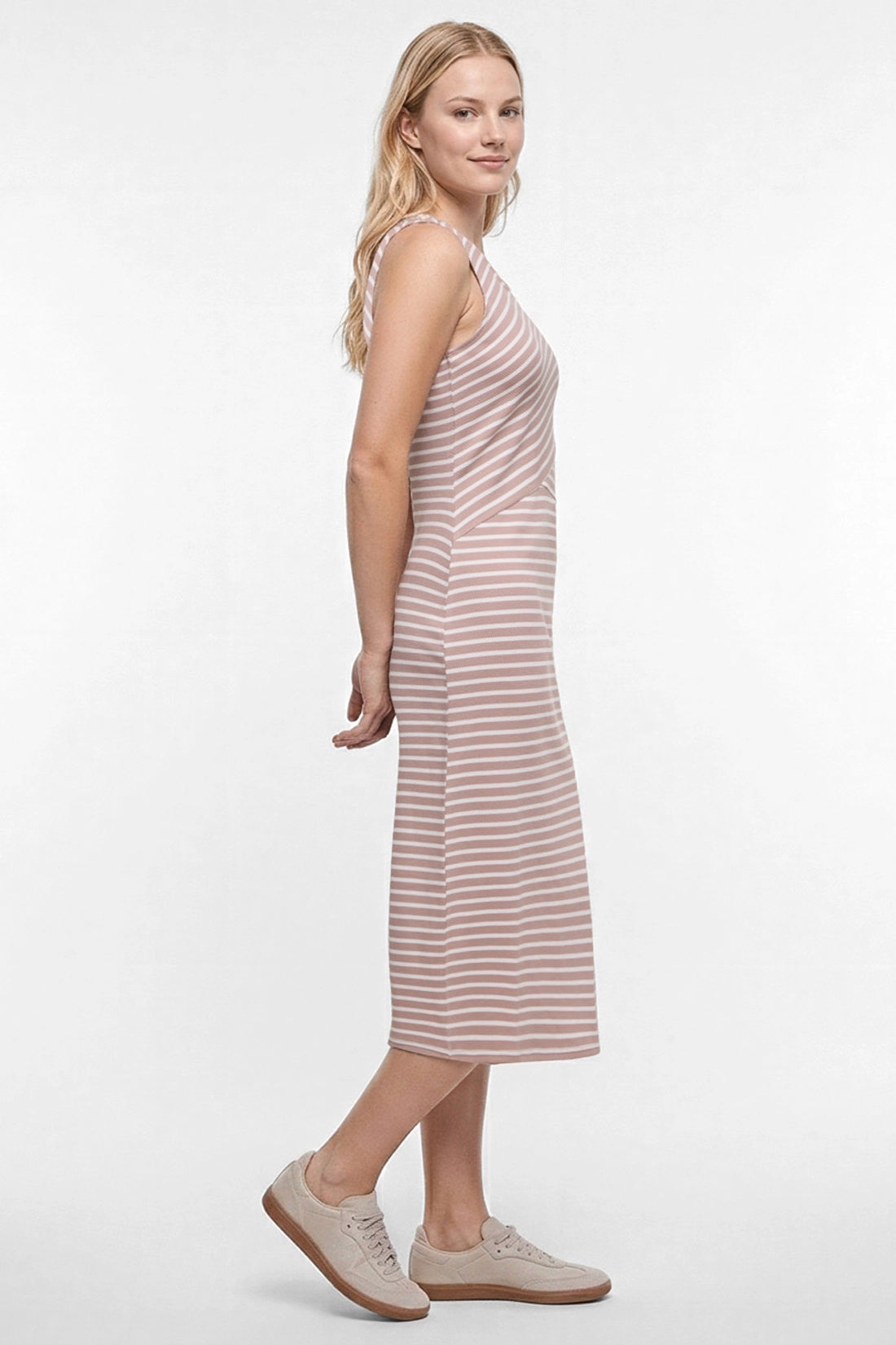 A woman modeling a sleeveless midi dress with horizontal light brown and white stripes, paired with beige sneakers, against a plain white studio background. 
