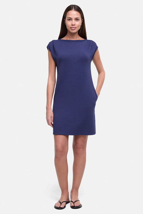 Woman wearing a royal blue dress with hand in pocket on a white background. #color_navy-academy