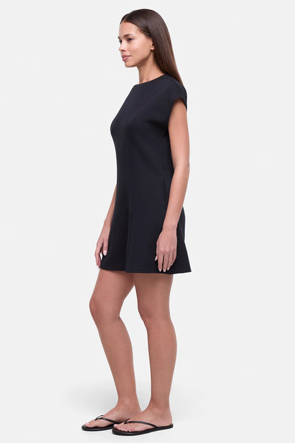 Side view of woman wearing a black mini dress on a white background.