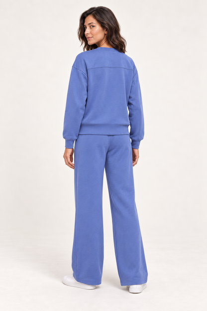 Woman wearing the blue Lana Pullover and matching pants, back studio view