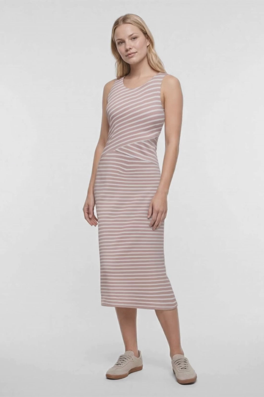 Video of a woman modeling a sleeveless midi dress with horizontal light brown and white stripes, paired with beige sneakers, against a plain white studio background. 