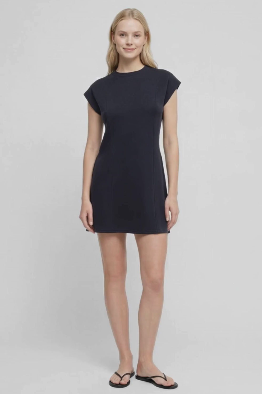 Video  view of woman wearing a black mini dress with hand in pocket on a white background. 