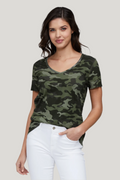 Woman wearing a camouflage t-shirt and white pants on a plain background